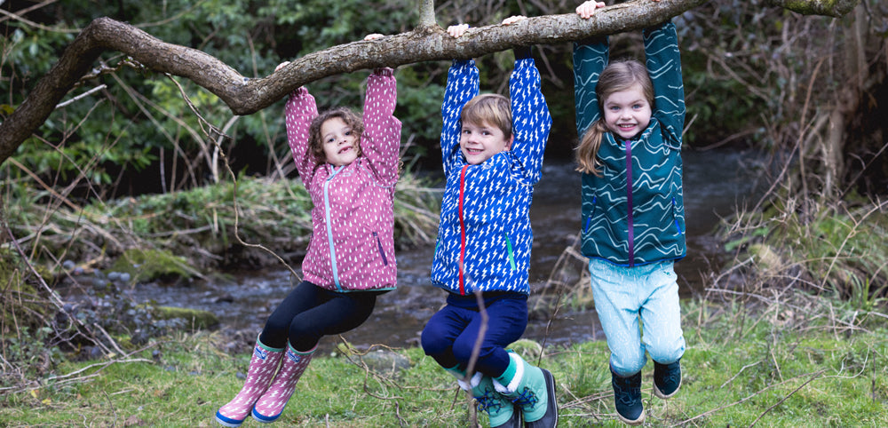 children swinging from tree branch wearing vibrant muddy puddles waterproof jackets and wellies