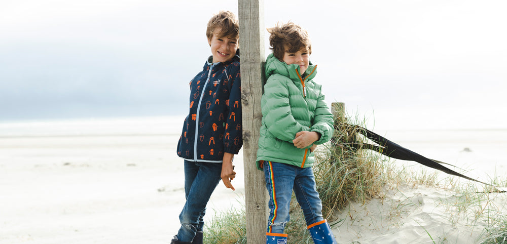 Boys on a sandy beach wearing Muddy Puddles waterproof jackets