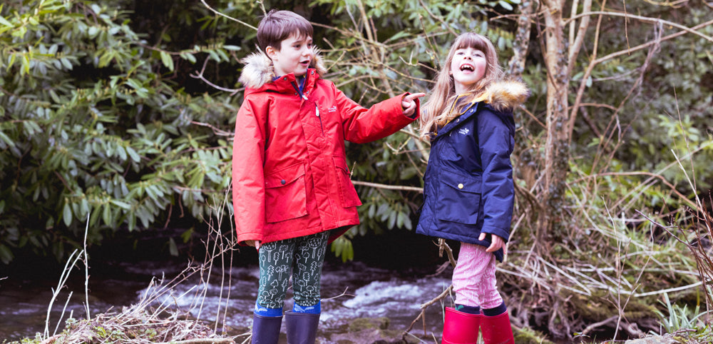 boy and girl stood in woodland area wearing red and navy muddy puddles parka jackets