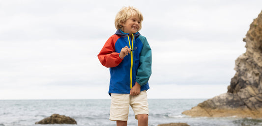 boy standing on beach laughing and wearing muddy puddles colourblock waterproof jacket