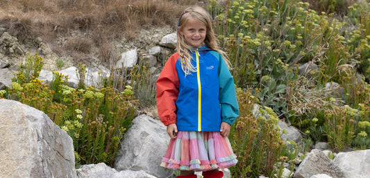 girl stood in front of rocky hillside wearing vibrant colourblock raincoat by muddy puddles