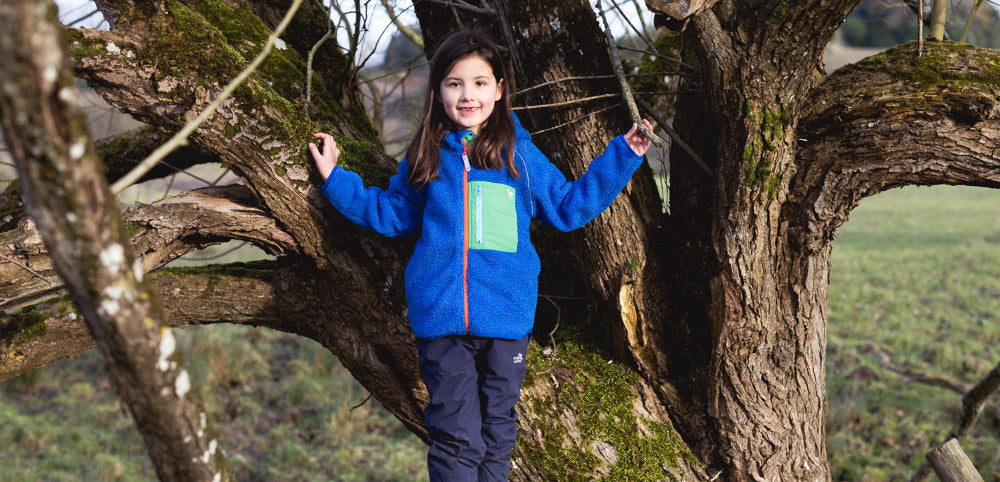 Child wearing waterproof outdoor clothing climbing a tree in a forest playground