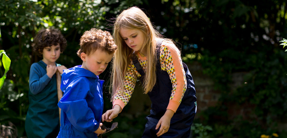 children gardening in a shady area, wearing muddy puddles waterproof dungarees and puddlesuits