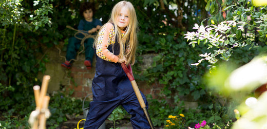 Child in waterproof outdoor clothing gardening with a spade in a lush backyard