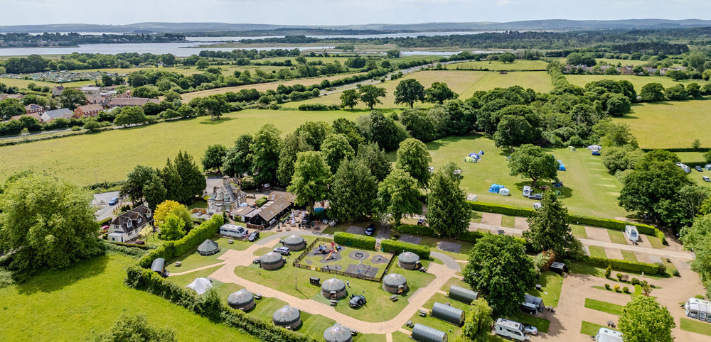 Aerial view of family glamping site with tents, caravans, and green countryside fields.