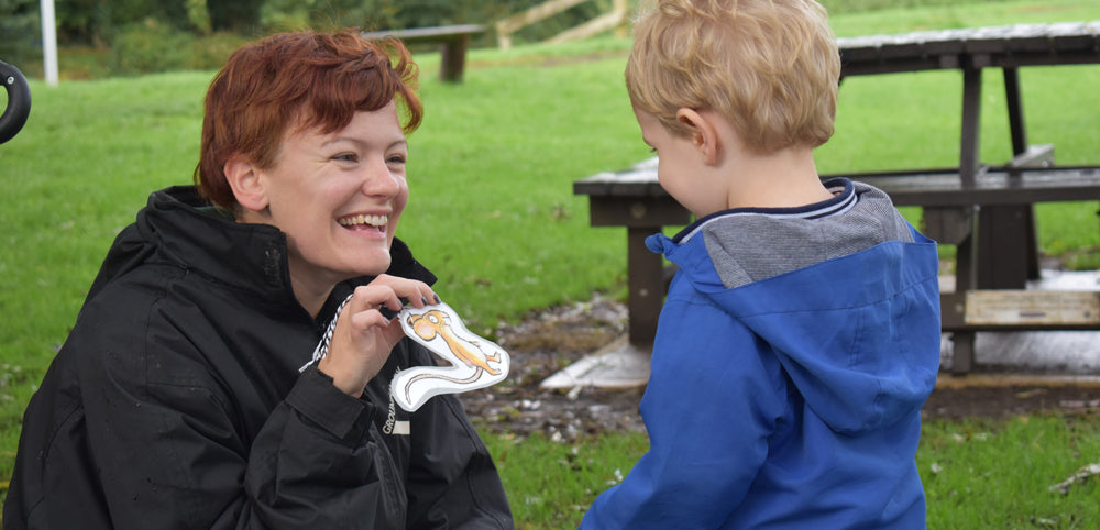Smiling woman engaging with young child in blue waterproof jacket outdoors on grass
