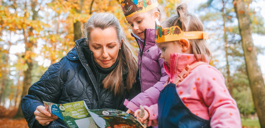 Mother and two children in waterproof jackets exploring outdoors, looking at a map in autumn forest