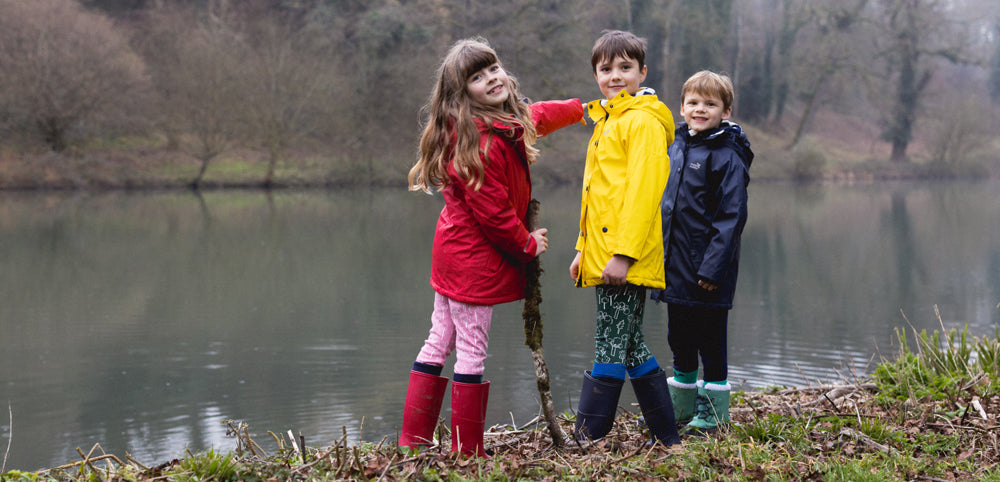 Children in colorful waterproof jackets and wellies by a lake in the outdoors
