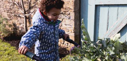 toddler boy pushing wheelbarrow full of leaves, wearing muddy puddles blue lightning print puddlesuit