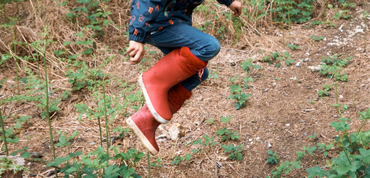 Child jumping outdoors wearing red waterproof boots and kids' rain jacket