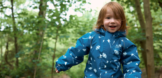 Child wearing blue waterproof jacket with white prints outdoors in a forest setting