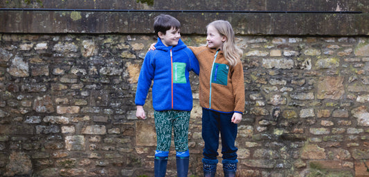 boy and girl stood in front of brick wall, wearing muddy puddles thermals and borg fleece jackets
