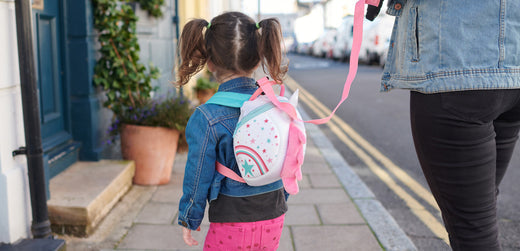 Young child in denim jacket with rainbow backpack walking on sidewalk, outdoor kidswear