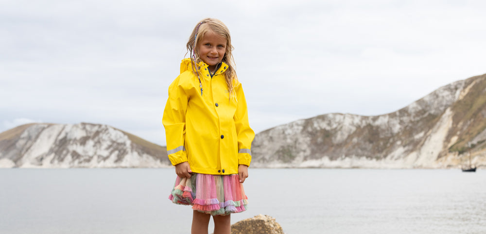 girl standing on beach wearing yellow muddy puddles waterproof jacket