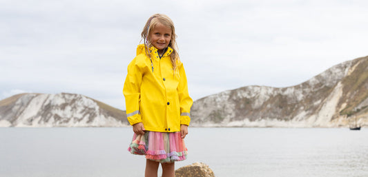 girl standing on beach wearing yellow muddy puddles waterproof jacket
