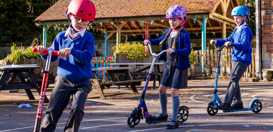 Children in school uniforms and helmets riding scooters outdoors on playground