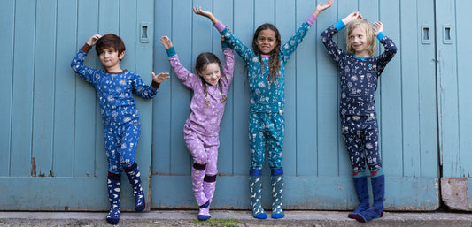 four children standing in front of blue doors wearing colourful thermals
