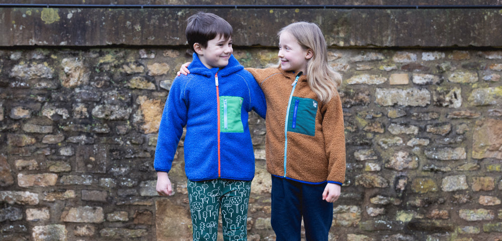 boy and girl stood in front of brick wall wearing muddy puddles borg fleece jackets and thermal baselayers