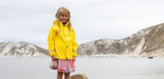 girl standing by the sea wearing bright yellow muddy puddles pu waterproof coat