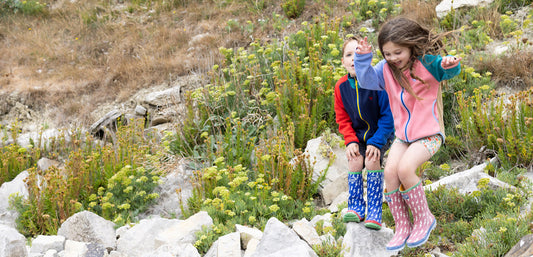 boy and girl wearing vibrant muddy puddles fleeces and wellies jumping off rocks