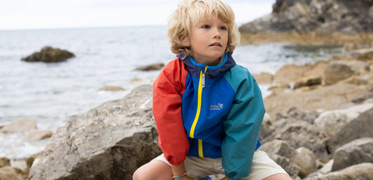 Child wearing colorful waterproof jacket on rocky beach, kids outdoor rainwear