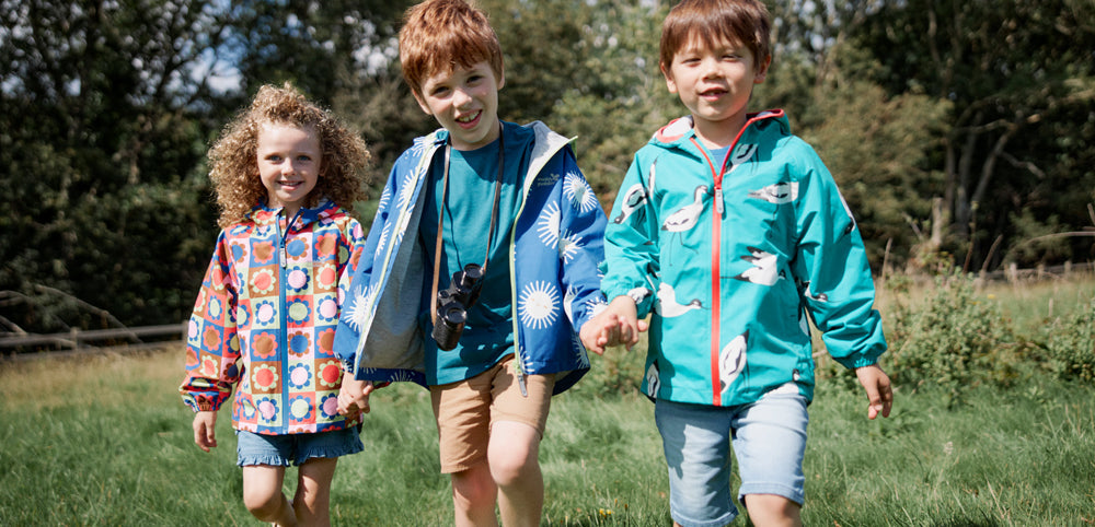 Three children in colorful waterproof jackets playing outdoors on green grass
