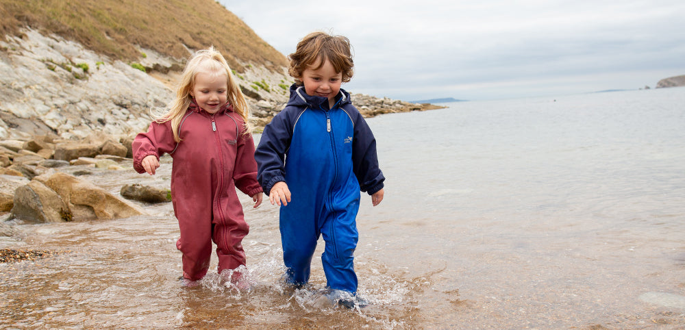 children walking through shallow water at the beach wearing vibrant pink and blue muddy puddles puddle suits