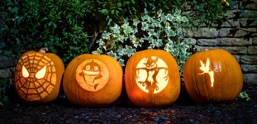 Four carved Halloween pumpkins with glowing faces and designs on a garden stone path