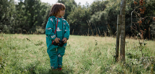 Child in turquoise waterproof rain suit standing in grassy field outdoors