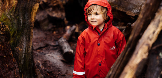 boy standing in rain in woodland area wearing muddy puddles red waterproof jacket