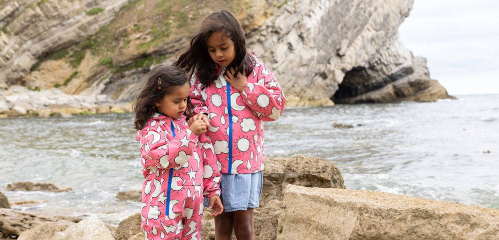 girls standing on beach wearing pink weather print muddy puddles waterproofs