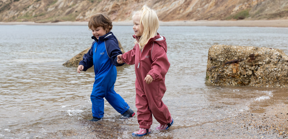 boy and girl paddling in the sea wearing muddy puddles softshell puddlesuits and wellies