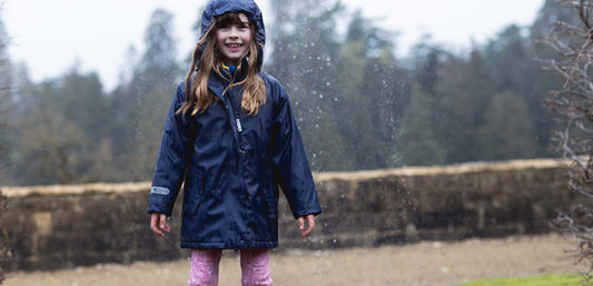 Child wearing navy waterproof jacket with hood outdoors in rainy weather
