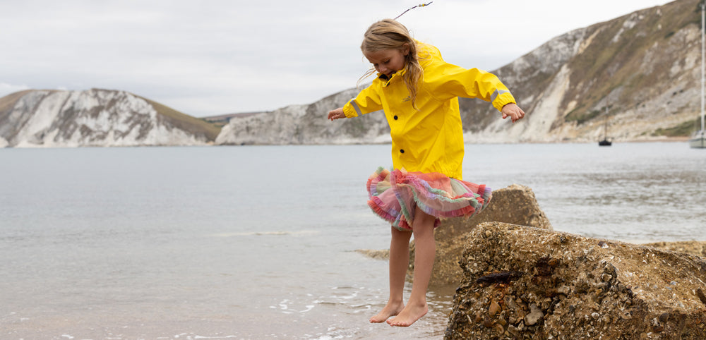 girl jumping into the sea wearing yellow muddy puddles waterproof jacket