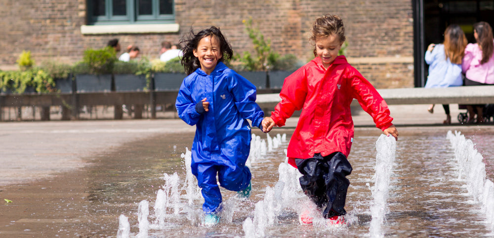 girls running through fountains, wearing vibrant muddy puddles waterproofs