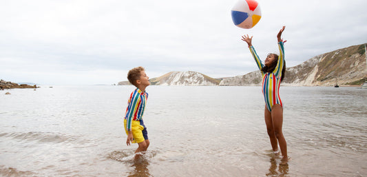 boy and girl in the sea wearing striped swimwear, playing with colourful beach ball