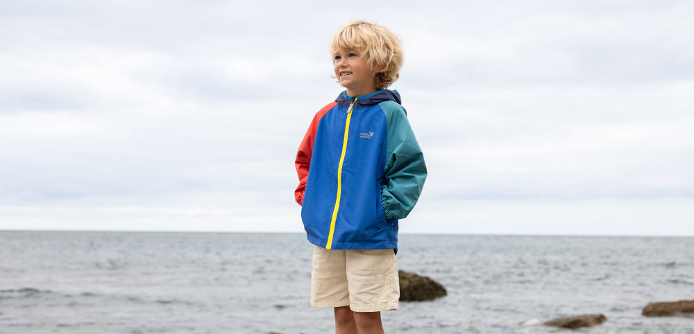 Child in a colorful waterproof jacket on a beach, kids outdoor clothing for rainy weather