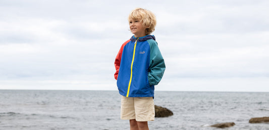 Child in a colorful waterproof jacket on a beach, kids outdoor clothing for rainy weather