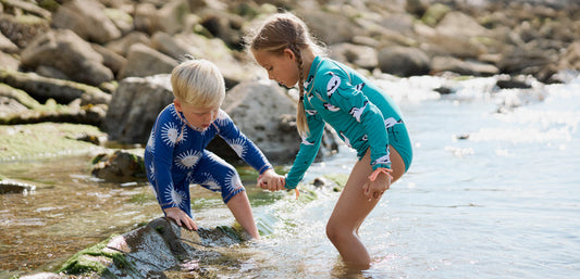 Two children in colorful swimwear playing on rocks and in shallow water outdoors