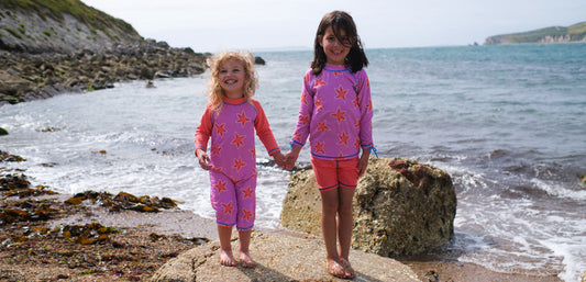 Children in colorful starfish swimwear standing on beach rocks by the sea