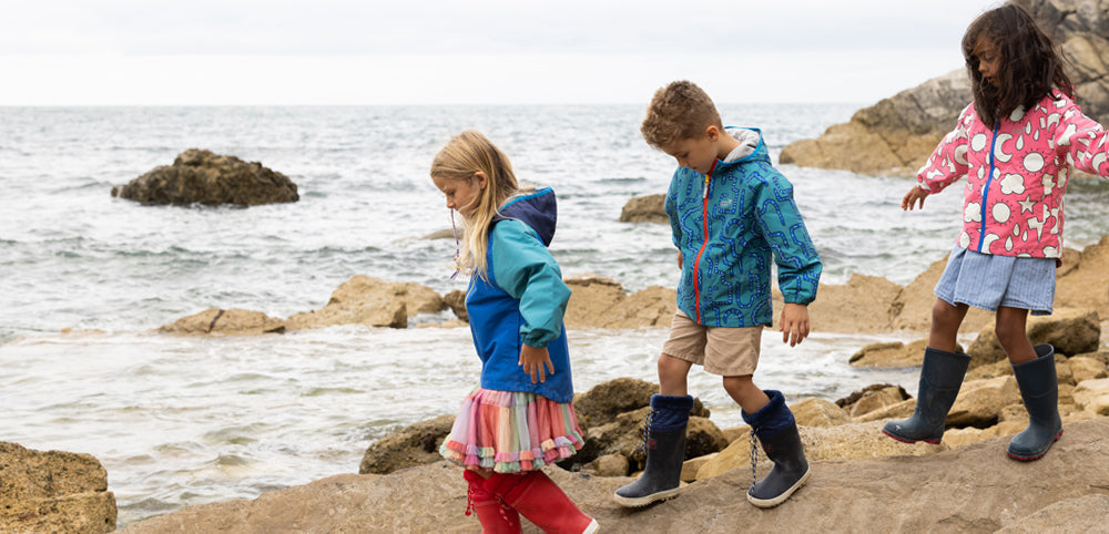 children walking over rocky beach wearing muddy puddles waterproof jackets