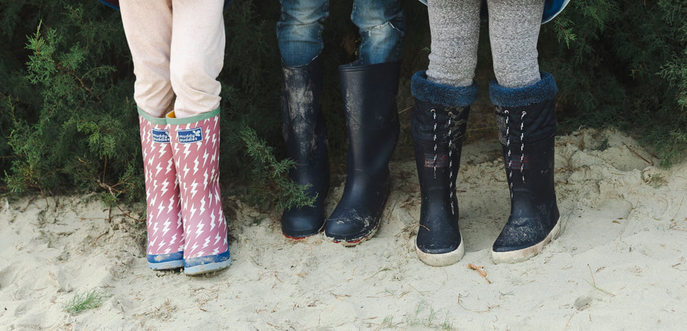 children stood on beach wearing muddy puddles wellies