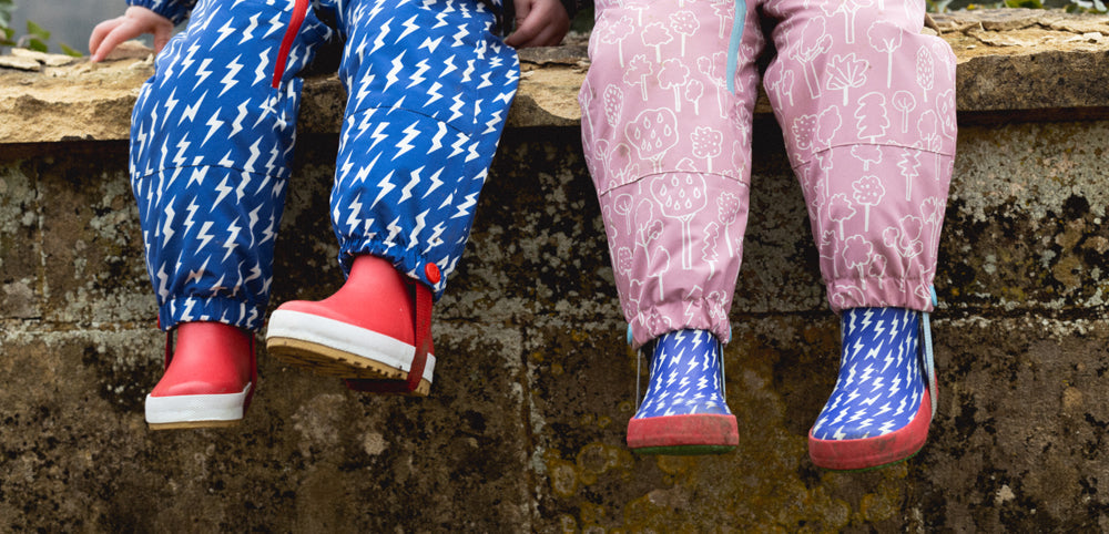 Children wearing colorful waterproof trousers and wellies sitting on a stone wall