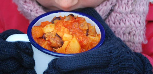 child holding white and blue enamel cup with vegetable stew