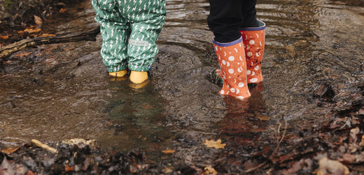 Children in waterproof trousers and rain boots standing in a muddy puddle outdoors