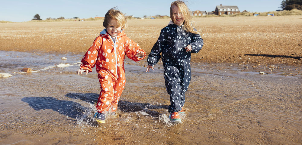 Children in polka dot waterproof rain suits playing and splashing at the beach