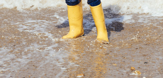 Child wearing yellow waterproof boots standing in shallow water on a sandy beach