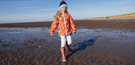 Child wearing waterproof jacket and wellies on beach, outdoor kids rainwear clothing