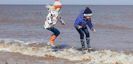 Children wearing waterproof coats and wellies jumping in waves on a beach