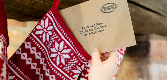 Hand holding envelope above red and white Christmas stocking with festive pattern